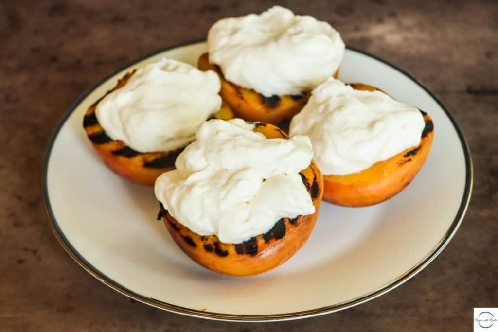 This is a picture of grilled peaches with fresh whipped cream.